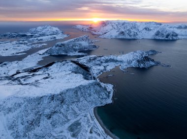 Nefes kesici karlı adalar ve okyanusu aydınlatan canlı bir günbatımının yer aldığı nefes kesici bir hava manzarası.