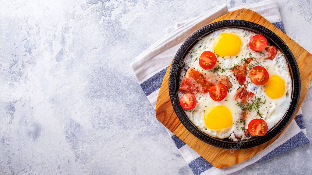 Morning breakfast concept: fried eggs with bacon and tomatoes. Top view, text space