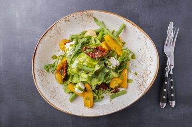 Peynirli balkabağı salatası ve çatal ve bıçakla servis edilen tabakta kurutulmuş domates. Sonbahar salatası. Üst görünüm
