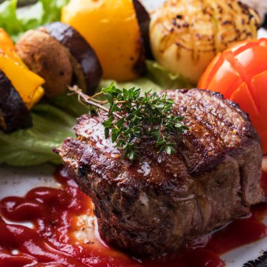 Biftek. Kırmızı soslu sulu orta boy biftek ve ızgara sebze. Yakın çekim.