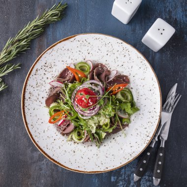 Çatal ve bıçakla servis edilen tabakta biftek ve sebzeli et salatası. Üst görünüm