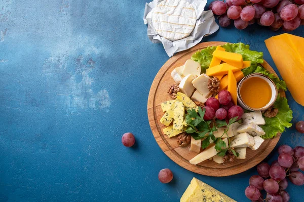 Delicious cheese board  with honey and red grape. Cheese appetizer on a wooden board.  Top view. Copy space.