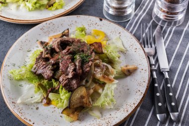 Izgara dana eti ve çatal ve bıçakla servis edilen taze sebzeli lezzetli salata..