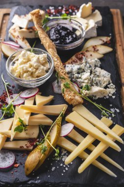 Siyah bir taşın üzerinde reçelli ve armutlu çeşitli peynirler.