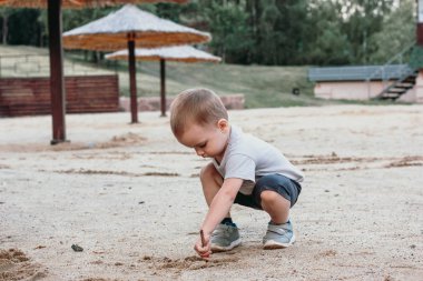 Küçük çocuk yaz kumsalında kumla oynuyor.