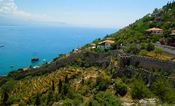 Muros de fortaleza e casas espalhadas na encosta verde descendo em direção ao mar Mediterrâneo azul com a linha de montanhas nebulosas no horizonte na cidade de Alanya. Antalya, Turquia . — Fotografia de Stock