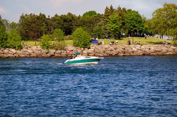 MISSISSAUGA, CANADÁ - 06 10 2020: Una lancha verde y blanca con bandera canadiense ondeando en las aguas del lago Ontario frente a la gente descansando en el Waterfront Trail — Foto de Stock