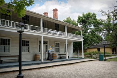 TORONTO, CANADA - 06: 21 2016: 19. yüzyıl kostümlü bir müze çalışanı, 1849 tarihli Black Creek Pioneer Village 'daki Half Way House Inn' den yürüyerek çıktı..