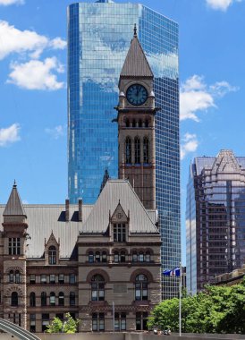 TORONTO, CANADA - 06 27 2016: Cadillac Fairview Kulesi 'nin camsı duvarının önündeki saat kulesi Nathan Phillips Meydanı' ndan görünen beyaz bulutlarla mavi gökyüzünü yansıtıyor