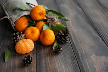 Noel ve yeni yıl atmosferini: taze mandalina yeşil yaprakları koyu ahşap arka plan üzerinde. Mandarin soyulmuş ve demonte dilimleri, tarçın, koniler, mandalina kabukları, yaprakları.