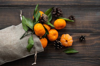 Noel ve yeni yıl atmosferini: taze mandalina yeşil yaprakları koyu ahşap arka plan üzerinde. Mandarin soyulmuş ve demonte dilimleri, tarçın, koniler, mandalina kabukları, yaprakları.