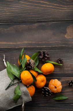 Noel ve yeni yıl atmosferini: taze mandalina yeşil yaprakları koyu ahşap arka plan üzerinde. Mandarin soyulmuş ve demonte dilimleri, tarçın, koniler, mandalina kabukları, yaprakları.