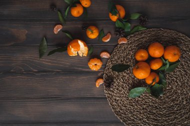 Noel ve yeni yıl atmosferini: taze mandalina yeşil yaprakları koyu ahşap arka plan üzerinde. Mandarin soyulmuş ve demonte dilimleri, tarçın, koniler, mandalina kabukları, yaprakları.