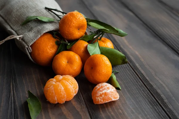 Noel ve yeni yıl atmosferini: taze mandalina yeşil yaprakları koyu ahşap arka plan üzerinde. Mandarin soyulmuş ve demonte dilimleri, tarçın, koniler, mandalina kabukları, yaprakları.