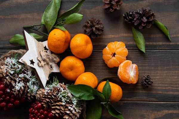 Noel ve yeni yıl atmosferini: taze mandalina yeşil yaprakları koyu ahşap arka plan üzerinde. Mandarin soyulmuş ve demonte dilimleri, tarçın, koniler, mandalina kabukları, yaprakları.