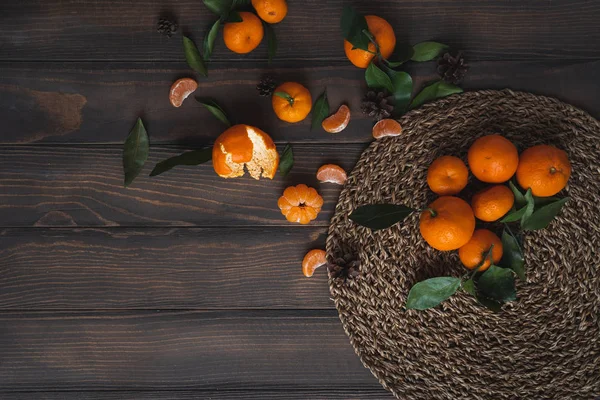 Noel ve yeni yıl atmosferini: taze mandalina yeşil yaprakları koyu ahşap arka plan üzerinde. Mandarin soyulmuş ve demonte dilimleri, tarçın, koniler, mandalina kabukları, yaprakları.
