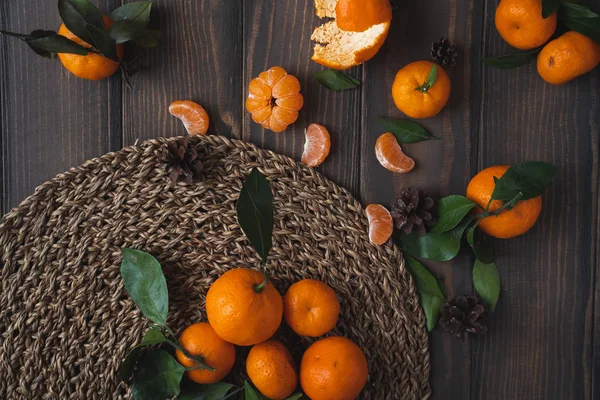 Noel ve yeni yıl atmosferini: taze mandalina yeşil yaprakları koyu ahşap arka plan üzerinde. Mandarin soyulmuş ve demonte dilimleri, tarçın, koniler, mandalina kabukları, yaprakları.