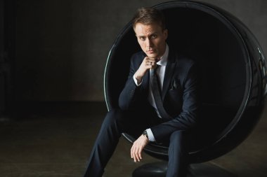 gri arka plan üzerinde sandalyede oturan genç işadamı