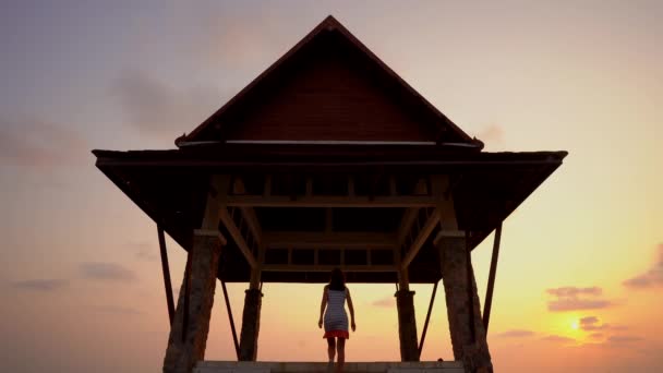 La fille va à l'océan dans un temple bouddhiste au coucher du soleil . — Video