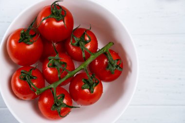 Beyaz ahşap zemin üzerinde bir tabak taze kiraz domates.