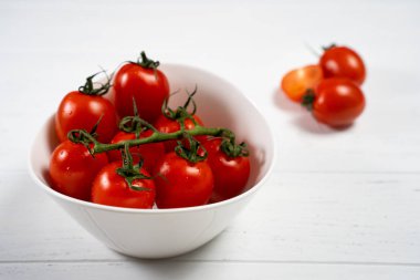 Beyaz ahşap zemin üzerinde bir tabak taze kiraz domates.