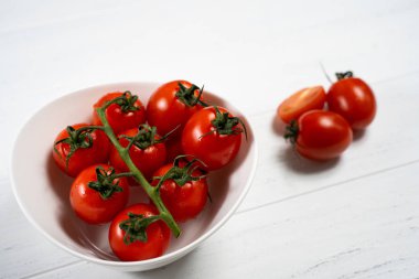 Beyaz ahşap zemin üzerinde bir tabak taze kiraz domates.