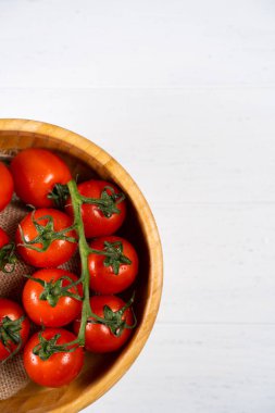 Beyaz ahşap zemin üzerinde ahşap bir tabak içinde taze kiraz domates.