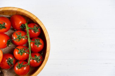 Beyaz ahşap zemin üzerinde ahşap bir tabak içinde taze kiraz domates.