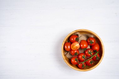 Beyaz ahşap zemin üzerinde ahşap bir tabak içinde taze kiraz domates.