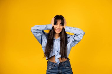 Mavi gömlekli genç bir kız sarı arka planda bir fotoğraf için poz veriyor..