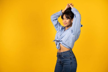 Mavi gömlekli genç bir kız sarı arka planda bir fotoğraf için poz veriyor..