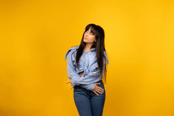 Joven hermosa chica en una camisa azul posando para una foto sobre un fondo amarillo . —  Fotos de Stock