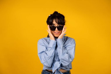 Güneş gözlüklü genç kız sarı arka planda fotoğraf için poz veriyor..