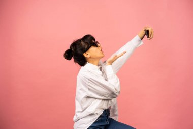 Güneş gözlüklü genç kız pembe arka planda selfie çekiyor..
