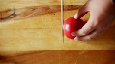Erkek elleri keskin bir bıçakla tahta bir tahtada taze sulu domatesleri kesiyor.