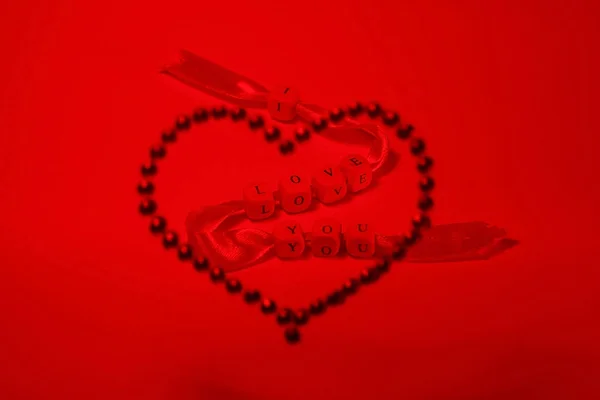A red tape with the inscription of love, like an arrow breaks a heart made of red rhinestones. Original lighting is a beautiful composition, a wonderful photo of the day of Sainted Valentine.