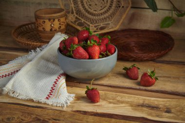 Natürmort hasır ware ahşap arka plan üzerinde bir gri kil kase çilek.