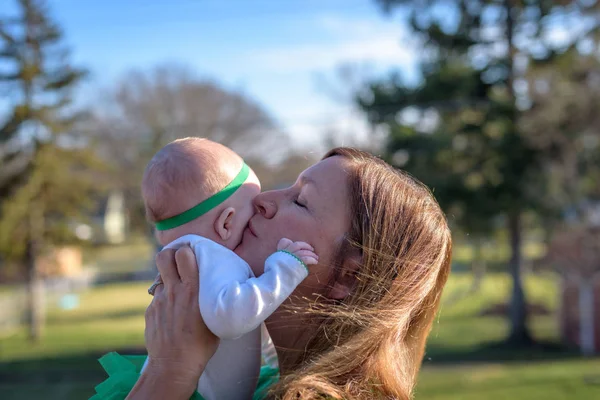 woman lifting babhy up in air to kiss outside on St. Patrick\'s Day