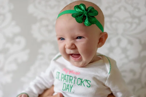 Büyük mavi gözlü gülüyor ve St Patricks Günü kıyafeti ve yonca kafa bandı giyen İrlandalı bebek