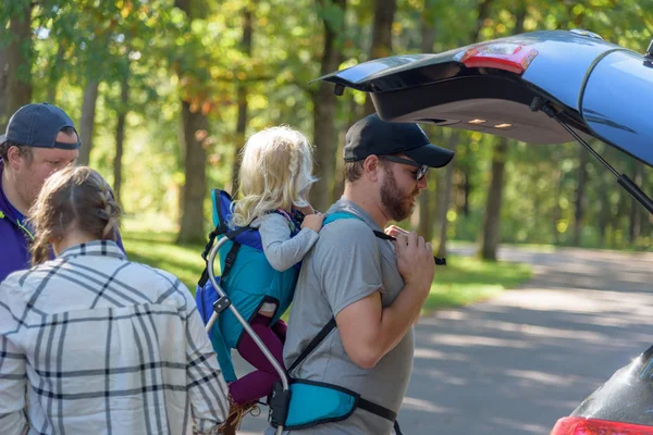 young family getting kid in backpack for a fall hike in the woods