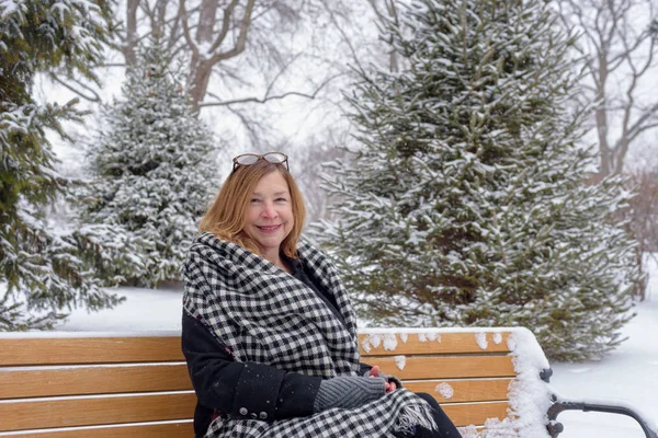 happy person sitting on park bench in winter with snow falling
