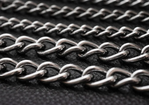 Metal silver chains on luxury black leather texture.