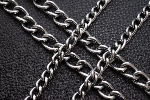 Metal silver chains on luxury black leather texture.