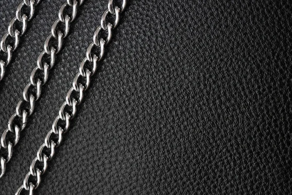 Metal silver chains on luxury black leather texture.