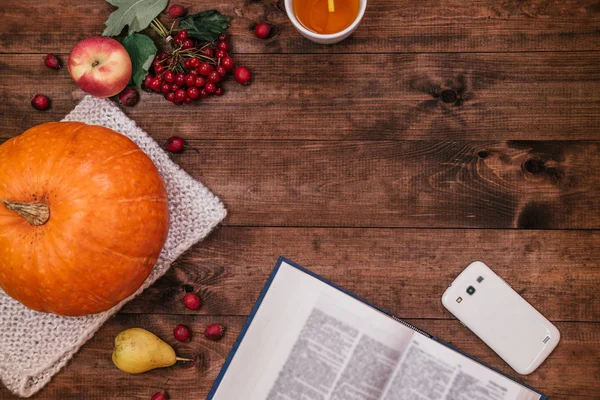 Top view of a  pumpkin, apples and a book, phone on wooden table.