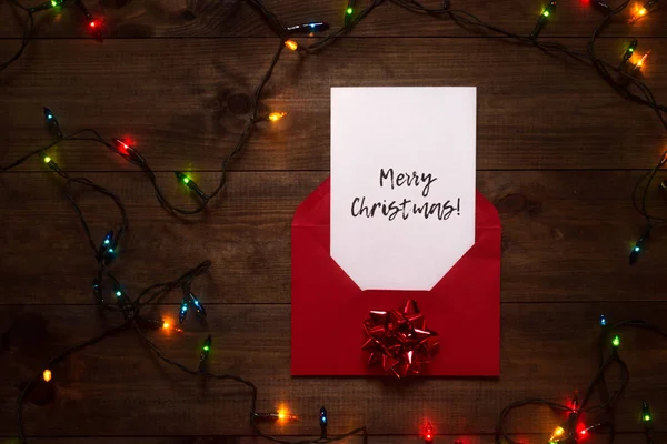 Letter with Christmas greeting and Christmas lights on a wooden table. Christmas time and New Year. Wishing Merry Christmas