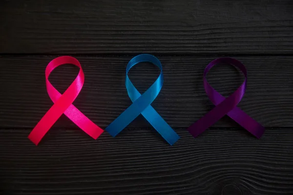 Close up of cancer ribbons on black wooden background. Cancer awareness month.