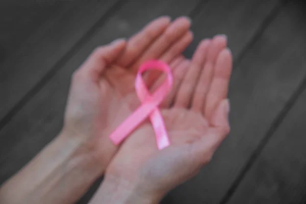 Womans hands holding pink ribbon on black wooden background, breast cancer awareness month, concept of health.