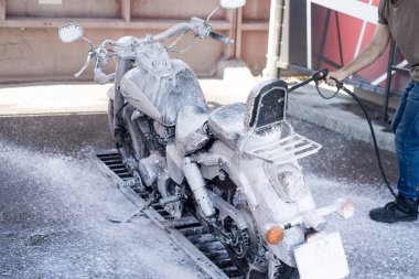 Adam su ve köpük ile oto yıkama bir motosiklet yıkar. 