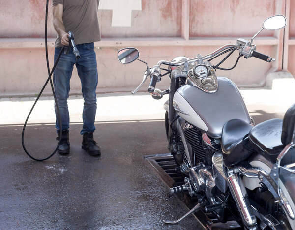 Man washes a motorbike at the car wash by water and foam. 